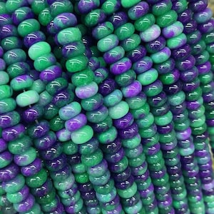 May include: Close-up of multiple strands of beads in shades of green and purple. The beads are oval-shaped and have a glossy finish. The color gradient creates a visually appealing pattern, suitable for jewelry making.