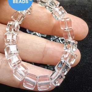May include: A strand of clear glass square beads. The beads are faceted and have a slight shimmer. The beads are strung on a white thread.