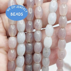 Puede incluir: Seis hilos de cuentas ovaladas, semitranslúcidas, de color morado claro y blanco. Un logotipo circular azul con el texto blanco WK DIY JEWERLY BEADS está superpuesto sobre los hilos. Las cuentas tienen un acabado liso y pulido y están ensartadas.
