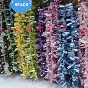 Può includere: Assortimento di perline di cristallo a punta iridescenti in vari colori, tra cui verde, blu, viola e rosa. Le perline sono disposte in file e numerate da 1 a 15.