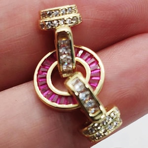 May include: Gold-toned earrings with a circular design featuring pink gemstones and clear crystals. The earrings have a post and a decorative top and bottom, with a central pink gemstone ring.