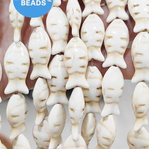 May include: Strands of off-white fish-shaped beads with brown markings. The beads are strung together, creating a flowing pattern. The image includes a blue circle with the text "wk DIY Jewelry BEADS".