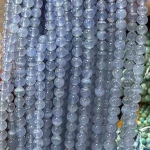 May include: A strand of light blue round beads, made of chalcedony, a type of quartz. The beads are smooth and translucent, with a slight shimmer. The strand is approximately 16 inches long.