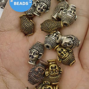 May include: A collection of silver and gold tone metal beads featuring a Buddha face design. The beads are textured and have a slightly distressed finish.  WK DIY Jewelry Beads.