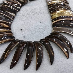 May include: A brown and gold shell necklace with a unique, pointed design. The necklace is made of many individual shell pieces that are arranged in a fan shape.