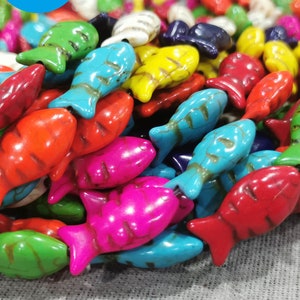 May include: A collection of colorful, fish-shaped beads in various shades of red, blue, green, yellow, and pink. The beads have a textured appearance and are likely made of stone or a similar material. These beads could be used for jewelry making or other craft projects.