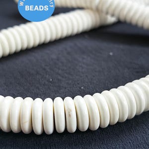 以下が含まれることがあります： 白いセラミックビーズのネックレス。各ビーズは丸く、わずかに平らになっているため、独特の質感があります。ビーズは糸でつなぎ合わせて、長いネックレスになっています。