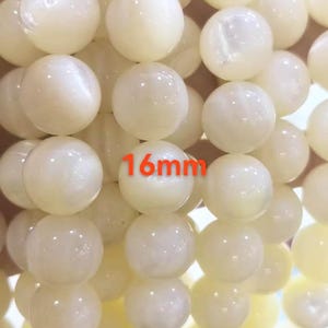 May include: Close-up of creamy white, round beads. The beads are strung together, with the text "16mm" in red. The beads have a smooth, polished surface, and are likely used for jewelry making or crafts.