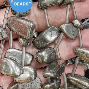 May include: A strand of silver-toned pyrite gemstone beads, each bead is a unique, irregular shape. The beads are strung on a silver wire and are ready for jewelry making.