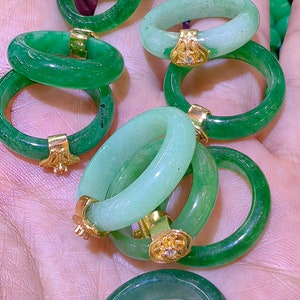 May include: A collection of jade rings with gold accents. The rings are various shades of green and are stacked on top of each other.