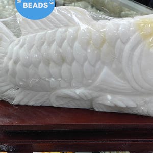 Può includere: Scultura di pesce bianco intagliata su una base di legno. Il pesce è dettagliato con squame e pinne. La scultura è avvolta nella plastica.