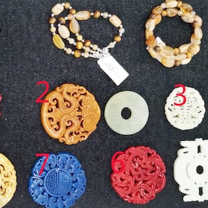Peut inclure: Une collection de 10 pendentifs en jade et en pierre, certains avec des sculptures complexes de dragons et d'autres motifs. Les pendentifs sont numérotés de 1 à 8 et sont présentés sur une surface noire.
