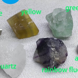May include: A collection of six different colored crystals, including green fluorite, yellow fluorite, rainbow fluorite, amethyst, blue stone, and rock quartz. The crystals are all natural and have a variety of shapes and sizes.