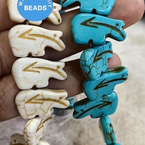 Op de afbeelding: Twee strengen turquoise en witte kralen met een pijlontwerp. De kralen hebben de vorm van een beer. De kralen zijn geregen aan een koord en klaar om te worden gebruikt voor het maken van sieraden. De kralen zijn gelabeld met "WK DIY Jewelry Beads".