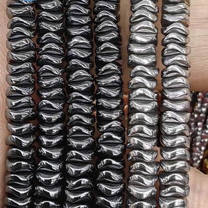 May include: A close-up of a strand of black hematite beads. The beads are faceted and have a shiny finish. The beads are arranged in a row and are being held by a hand. The text "DIY Jewelry Beads" is visible in the image.