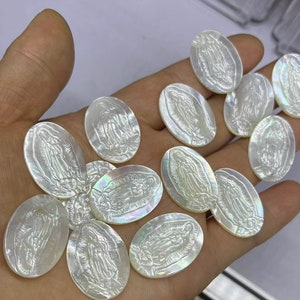 Puede incluir: Una colección de dijes de madreperla blanca de forma ovalada con una imagen grabada de la Virgen María.