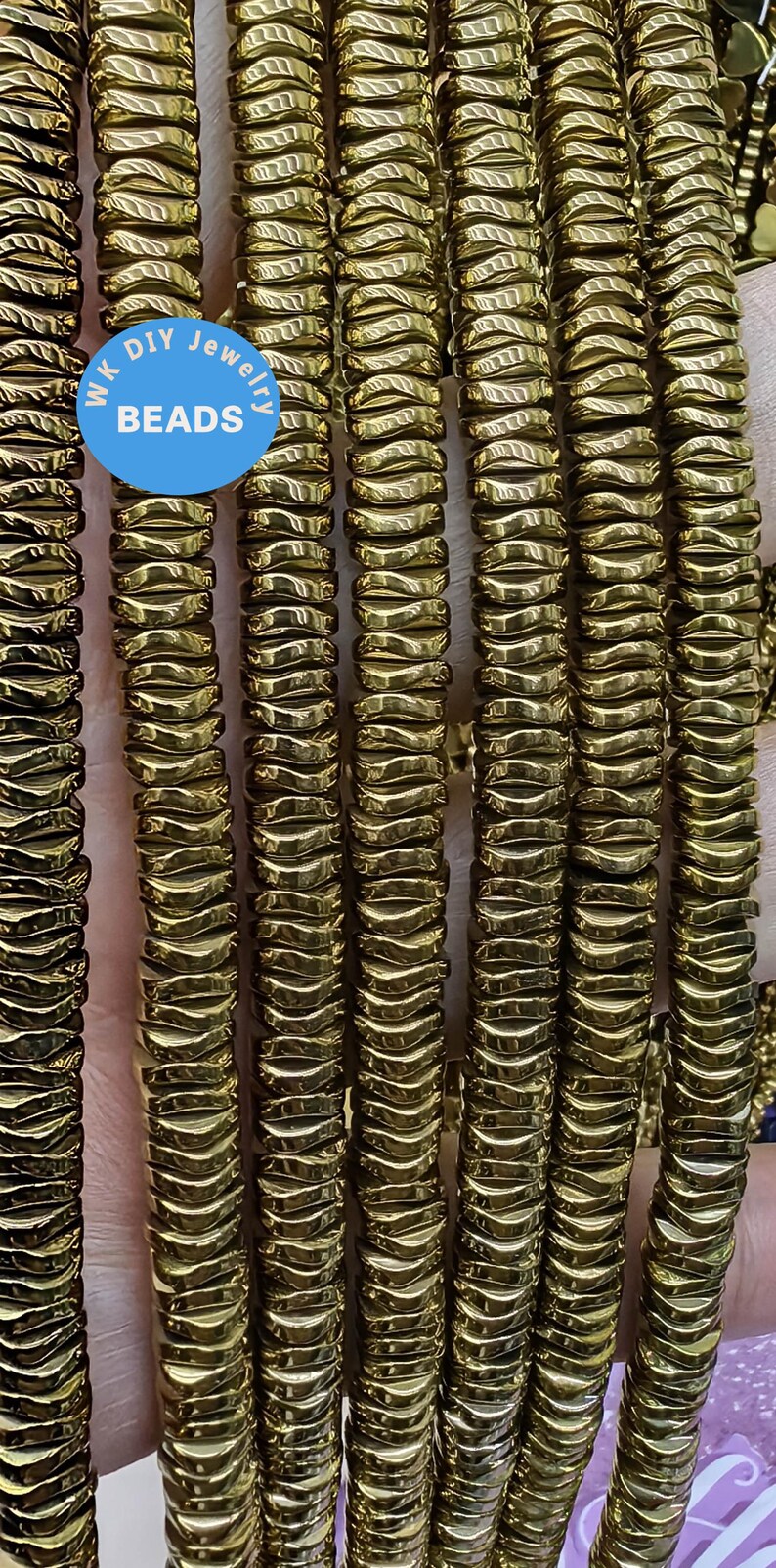 May include: A close-up of multiple strands of gold-toned hematite beads. The beads are faceted and have a wavy, textured surface. The beads are arranged in rows, creating a visual pattern.  WK DIY Jewelry Beads.