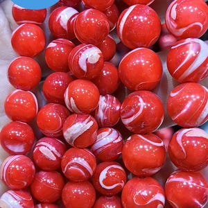 May include: A strand of red and white swirl beads. The beads are round and have a glossy finish. The beads are strung on a clear string.