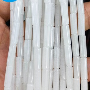 Könnte beinhalten: Nahaufnahme von Strängen aus weißen, zylindrischen Perlen. Die Perlen sind gleichmäßig geformt und groß, mit einer glatten, undurchsichtigen Oberfläche. Das Bild enthält einen blauen Kreis mit dem Text "DIY Jewelry BEADS".