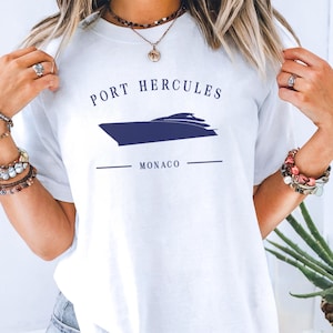 May include: White t-shirt with a navy blue graphic of a boat and the text "PORT HERCULES MONACO". The shirt is a crew neck style.