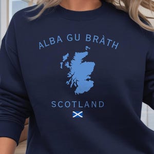 Puede incluir: Sudadera azul marino con las palabras "ALBA GU BRÀTH" y "SCOTLAND" en azul claro. También presenta un mapa de Escocia y una bandera escocesa en azul claro.