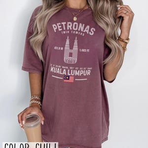 Peut inclure: Un t-shirt couleur chili avec un motif blanc des tours Petronas &agrave; Kuala Lumpur. L'impression comprend le texte Petronas Twin Towers, 451.9 M, 1 483 FT, des coordonn&eacute;es, Kuala Lumpur et un petit graphique du drapeau de la Malaisie.