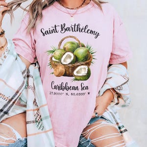 K&ouml;nnte beinhalten: Rosafarbenes T-Shirt mit einer Grafik eines Kokosnusskorbs und dem Text "Saint Barth&eacute;lemy Caribbean Sea". Das Shirt zeigt die Koordinaten 17.9000&deg; N, 62.8333&deg; W.