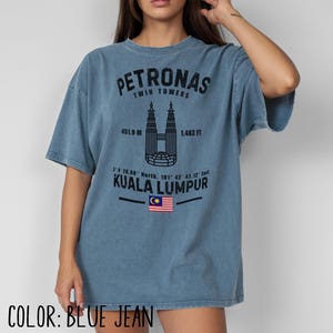 Peut inclure: Un t-shirt bleu jean avec un motif noir repr&eacute;sentant les tours Petronas de Kuala Lumpur. Le design comprend le texte Petronas Twin Towers, 451.9 M, 1,483 FT, des coordonn&eacute;es g&eacute;ographiques, Kuala Lumpur et un petit drapeau malaisien.