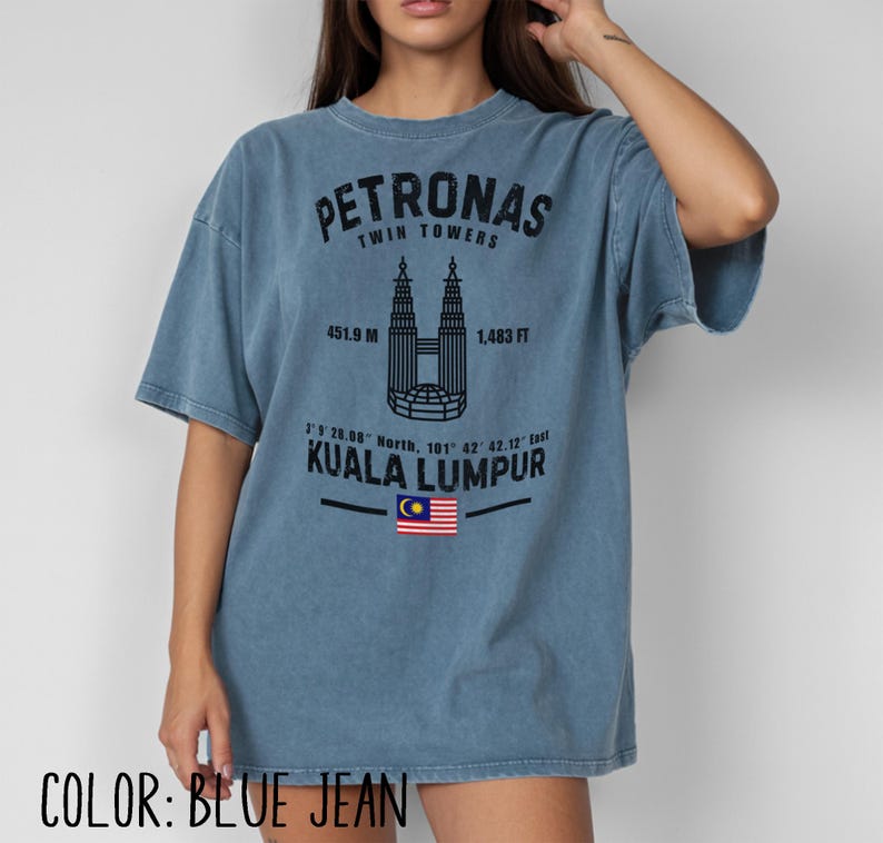 Peut inclure: Un t-shirt bleu jean avec un motif noir repr&eacute;sentant les tours Petronas de Kuala Lumpur. Le design comprend le texte Petronas Twin Towers, 451.9 M, 1,483 FT, des coordonn&eacute;es g&eacute;ographiques, Kuala Lumpur et un petit drapeau malaisien.