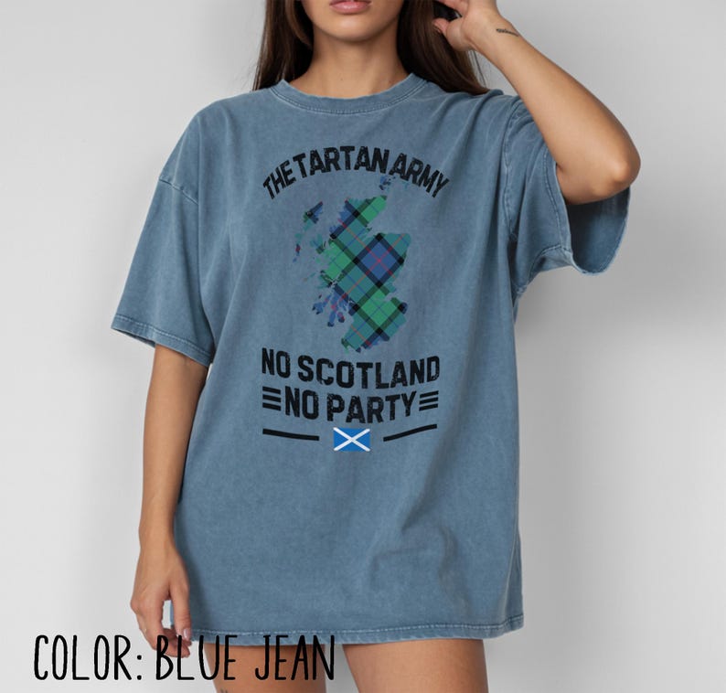 May include: A blue jean colored t-shirt featuring a graphic of the map of Scotland filled with a green and blue tartan pattern. The text reads THE TARTAN ARMY, NO SCOTLAND NO PARTY, and includes a small graphic of the Scottish flag with horizontal lines.