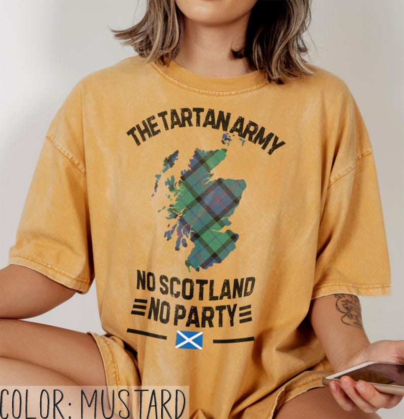 May include: A mustard yellow short-sleeve t-shirt featuring a graphic of the map of Scotland filled with a green, blue, and red tartan pattern. The text reads THE TARTAN ARMY, NO SCOTLAND NO PARTY, and includes a small blue and white Scottish flag.