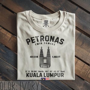 Peut inclure: Un t-shirt ivoire avec un motif noir repr&eacute;sentant les tours Petronas de Kuala Lumpur. Le design comprend le texte PETRONAS TWIN TOWERS, 451,9 M, 1 483 FT, des coordonn&eacute;es, KUALA LUMPUR et un petit drapeau malaisien au centre en bas.