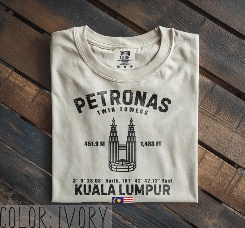 Peut inclure: Un t-shirt ivoire avec un motif noir repr&eacute;sentant les tours Petronas de Kuala Lumpur. Le design comprend le texte PETRONAS TWIN TOWERS, 451,9 M, 1 483 FT, des coordonn&eacute;es, KUALA LUMPUR et un petit drapeau malaisien au centre en bas.