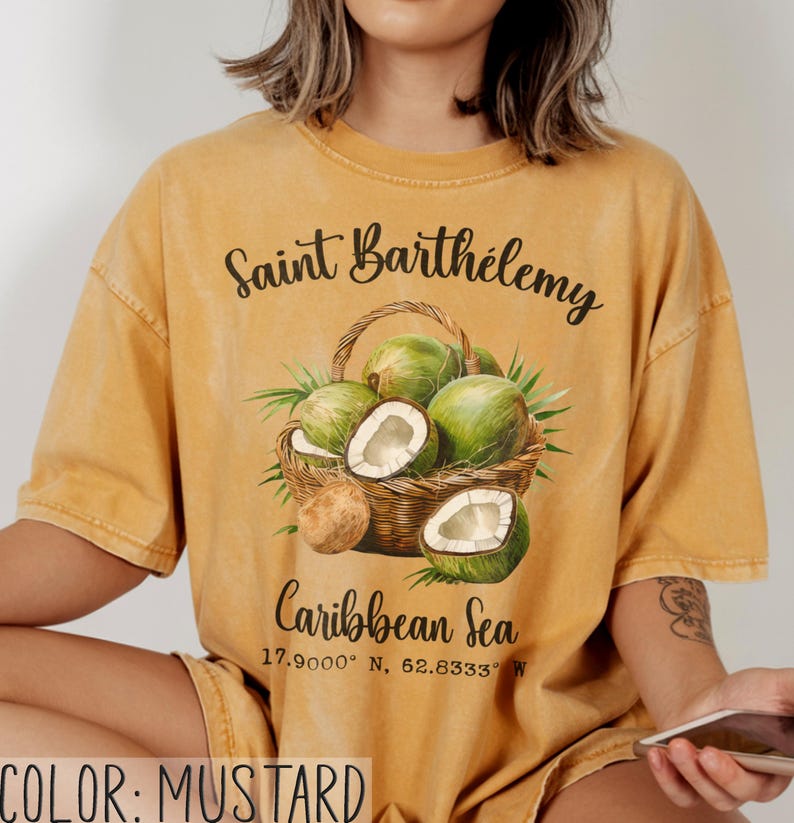 K&ouml;nnte beinhalten: Senffarbenes T-Shirt mit einer Grafik eines Korbes voller gr&uuml;ner Kokosn&uuml;sse und Palmenbl&auml;tter. Der Text auf dem Shirt lautet "Saint Barth&eacute;lemy" und "Caribbean Sea" mit Koordinaten. Das Shirt hat eine lockere Passform.