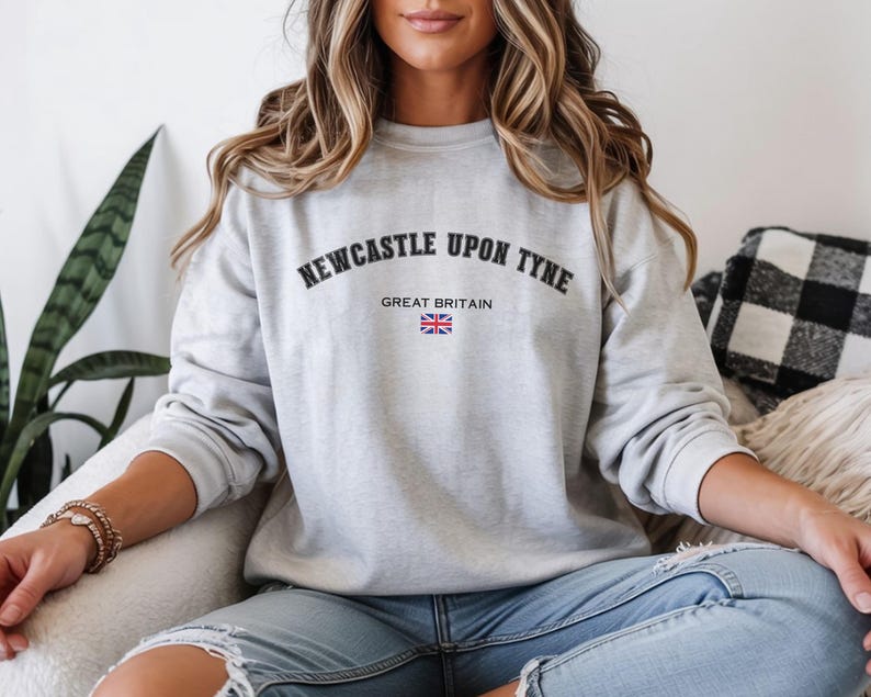 May include: A light gray sweatshirt with the text "NEWCASTLE UPON TYNE" arched across the top and "GREAT BRITAIN" below, with a small Union Jack flag. The sweatshirt is a crew neck style.