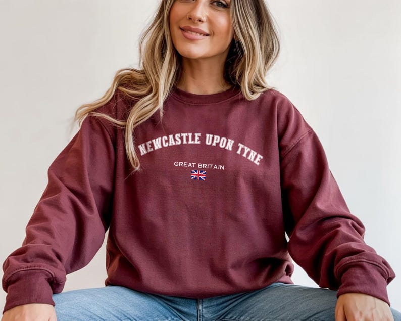 May include: Burgundy sweatshirt with the text "Newcastle Upon Tyne" in white arched lettering, with "Great Britain" and a Union Jack flag underneath. The sweatshirt has long sleeves and a crew neck.