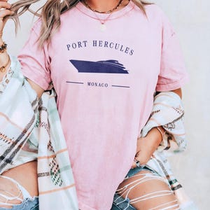 May include: A light pink t-shirt with the text "PORT HERCULES MONACO" and a navy blue boat graphic. The shirt is a soft, comfortable material.