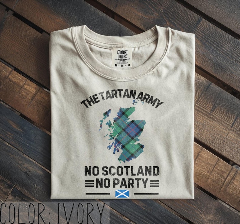 May include: An ivory short-sleeve t-shirt featuring a graphic of the map of Scotland filled with a green and blue tartan pattern. The text reads THE TARTAN ARMY, NO SCOTLAND NO PARTY, and includes a small blue and white Scottish flag icon.