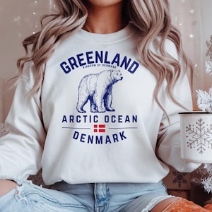 May include: White sweatshirt with a blue graphic of a polar bear and the words "GREENLAND" and "ARCTIC OCEAN DENMARK". The sweatshirt also features the flag of Denmark. The sweatshirt is a crew neck style.