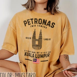 Peut inclure: Un t-shirt &agrave; manches courtes jaune moutarde avec un motif noir des tours Petronas de Kuala Lumpur. Le design comprend le texte Petronas Twin Towers, 451,9 m, 1 483 ft, des coordonn&eacute;es, Kuala Lumpur et un petit drapeau de la Malaisie.