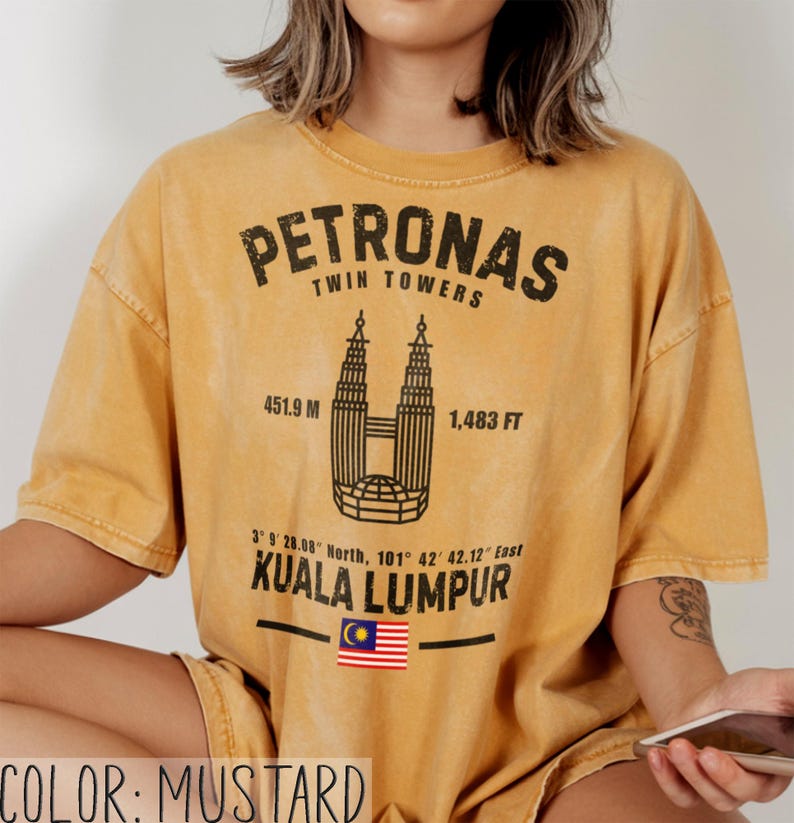 Peut inclure: Un t-shirt &agrave; manches courtes jaune moutarde avec un motif noir des tours Petronas de Kuala Lumpur. Le design comprend le texte Petronas Twin Towers, 451,9 m, 1 483 ft, des coordonn&eacute;es, Kuala Lumpur et un petit drapeau de la Malaisie.