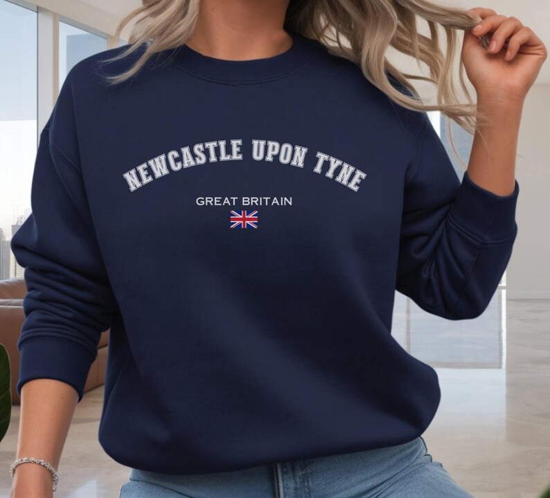 May include: Navy blue sweatshirt with the text "NEWCASTLE UPON TYNE" in white arched lettering. Below the text is "GREAT BRITAIN" and a small Union Jack flag. The sweatshirt is a solid color and has a crew neck.