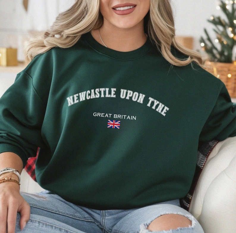 May include: Dark green sweatshirt with the text "NEWCASTLE UPON TYNE" in white arched lettering. Below the text is "GREAT BRITAIN" and a small Union Jack flag. The sweatshirt is a crew neck style.