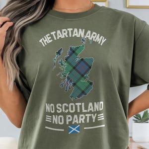 May include: A moss green t-shirt featuring a graphic of the map of Scotland filled with a blue, green, and black tartan pattern. The text reads THE TARTAN ARMY above the map and NO SCOTLAND NO PARTY below, with a small Scottish flag icon at the bottom.