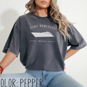 May include: Pepper-colored t-shirt with a white graphic of a yacht and the text "PORT HERCULES MONACO". The shirt has short sleeves and a relaxed fit. The color is displayed at the bottom of the image.