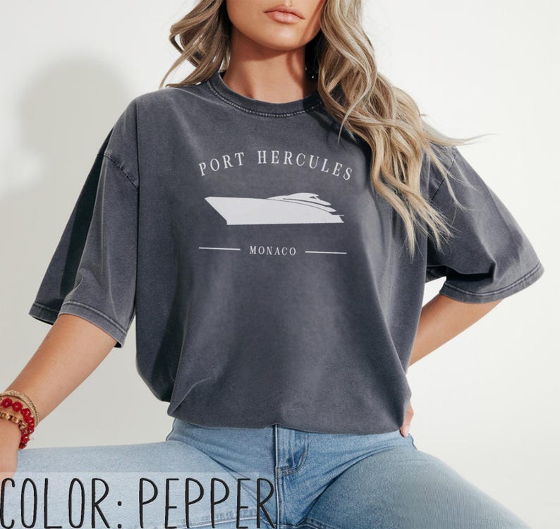 May include: Pepper-colored t-shirt with a white graphic of a yacht and the text "PORT HERCULES MONACO". The shirt has short sleeves and a relaxed fit. The color is displayed at the bottom of the image.