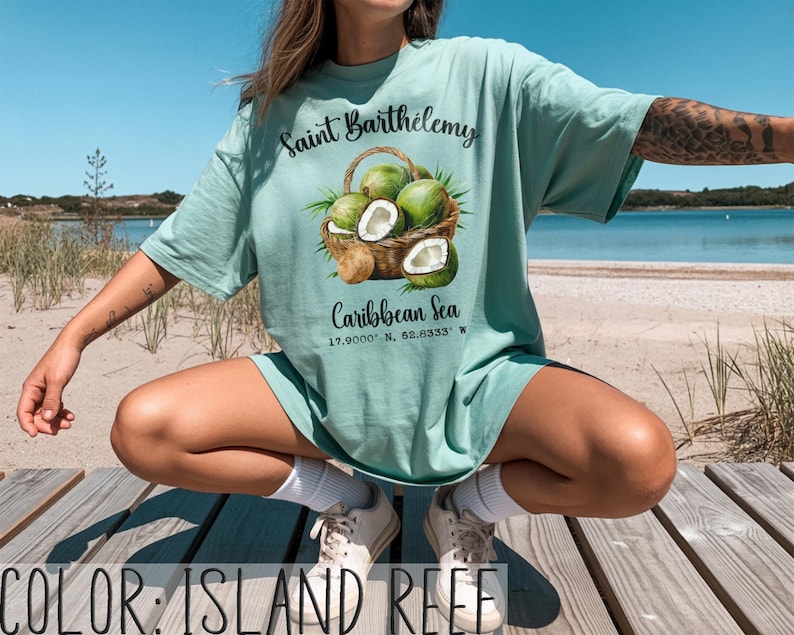 K&ouml;nnte beinhalten: Hellgr&uuml;nes T-Shirt mit dem Text "Saint Barth&eacute;lemy" &uuml;ber einer Grafik eines Korbes voller Kokosn&uuml;sse. Darunter steht "Caribbean Sea" und Koordinaten. Das Shirt ist einfarbig.