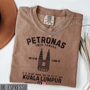 Peut inclure: Un t-shirt couleur espresso avec un motif noir des tours Petronas, le texte Petronas Twin Towers, 451.9 M, 1,483 FT, des coordonn&eacute;es, Kuala Lumpur et un petit drapeau malaisien. Le t-shirt porte une &eacute;tiquette de col de la marque Comfort Colors.