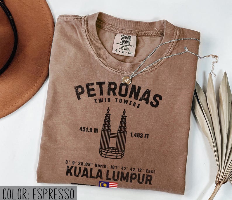 Peut inclure: Un t-shirt couleur espresso avec un motif noir des tours Petronas, le texte Petronas Twin Towers, 451.9 M, 1,483 FT, des coordonn&eacute;es, Kuala Lumpur et un petit drapeau malaisien. Le t-shirt porte une &eacute;tiquette de col de la marque Comfort Colors.