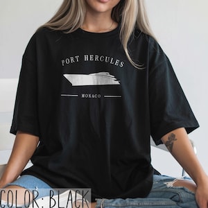 May include: Black t-shirt with a white graphic of a yacht and the text "PORT HERCULES MONACO". The shirt is a casual style, suitable for everyday wear.